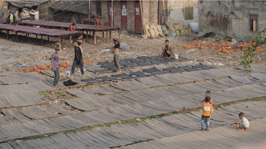 A photo of a neighbourhood in Dhaka. There is a group of men laying leather hides on flat surface. 