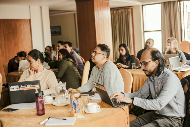 A photo of people in a conference room, sat in circle tables. 