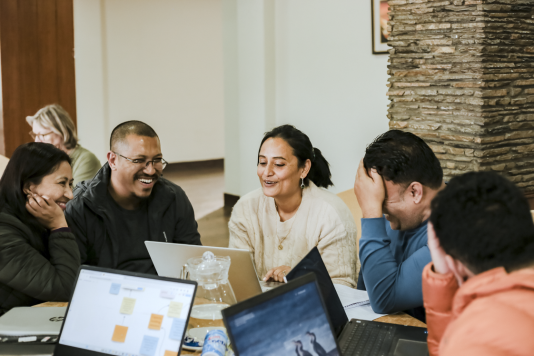 A photo of four people sat around a desk looking at laptops.