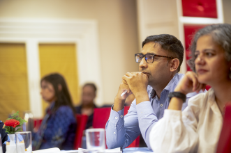 A photo of two people sat in a conference room, listening to a speaker.