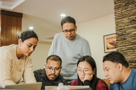 A photo of five people standing around a laptop screen, working collaboratively.