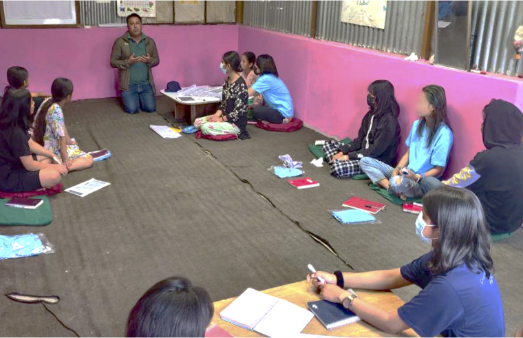 A photo of people sat on the floor, listening to a country coordinator