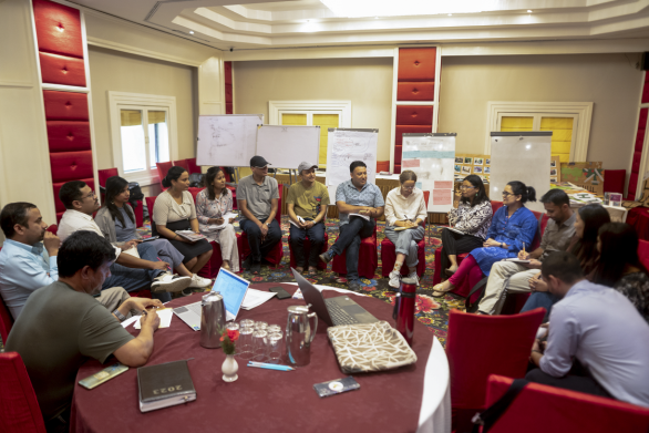 A photo of people sitting around in a circle in a conference room.